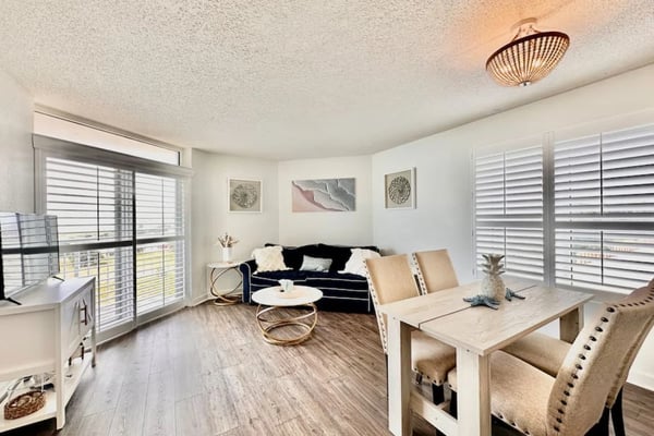 Bright beachfront condo living room with ocean view, gray sofa, dining area, and wood-look flooring