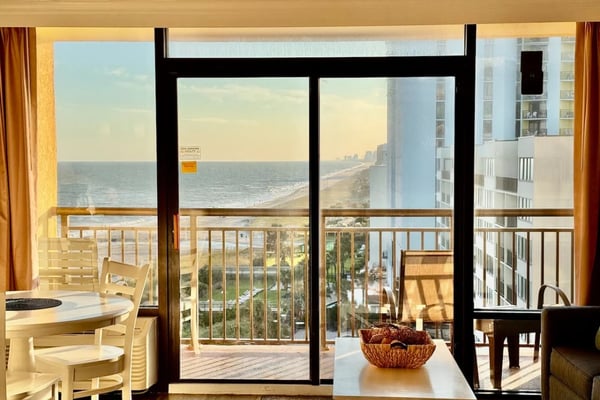 Four-panel collage showing bedroom with tropical wallpaper, kitchen with stainless steel appliances, dining area with ocean view, and bedroom with balcony